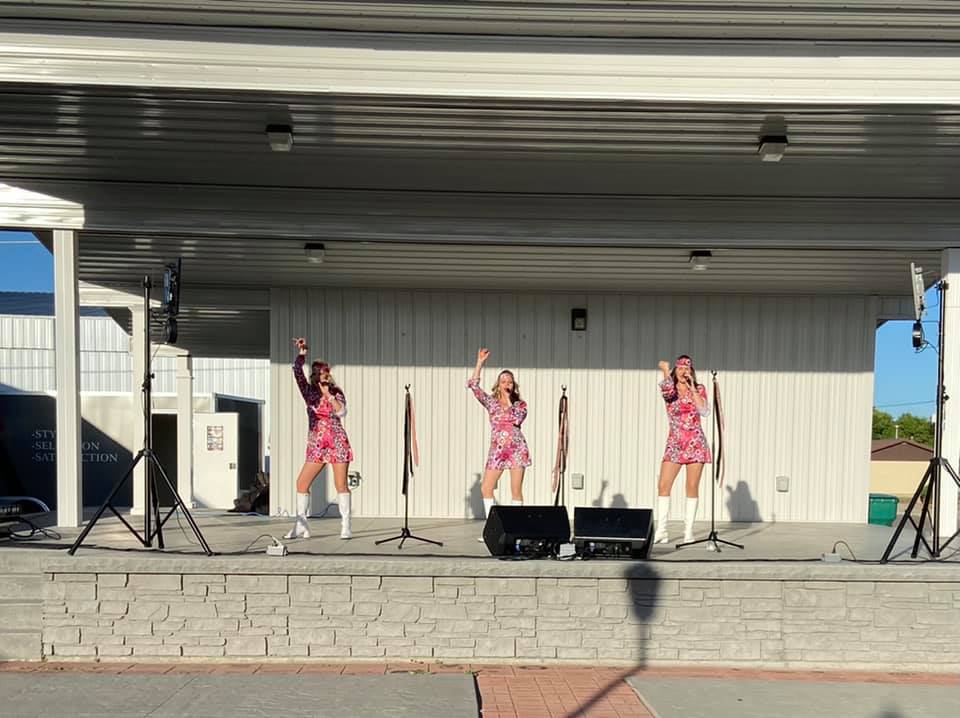 photo of three ladies dancing and singing on an outdoor stage